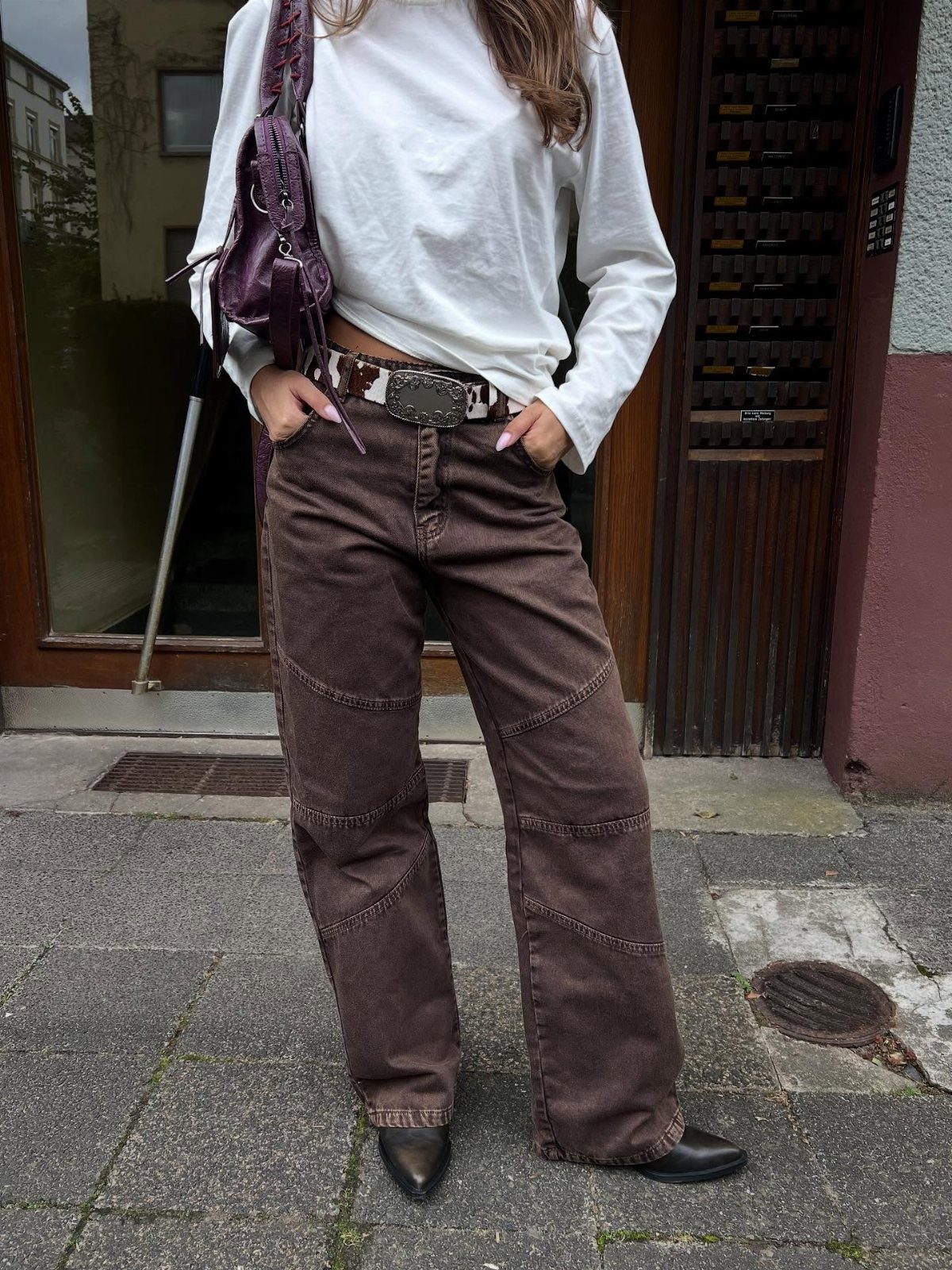 Person wearing brown bootcut jeans with a white top and cow-print belt.