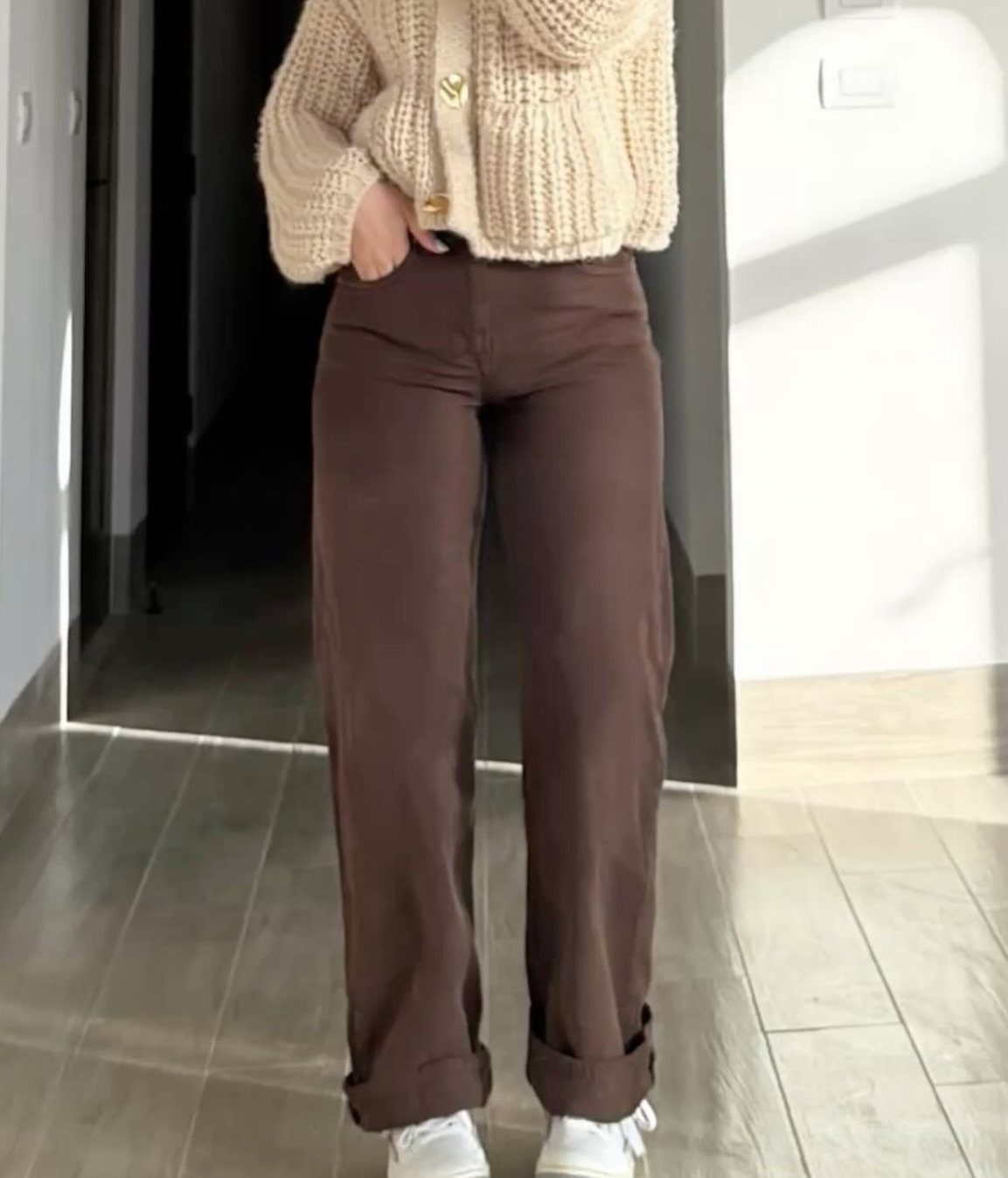 Brown wide-leg jeans paired with a cream knit cardigan and white sneakers.