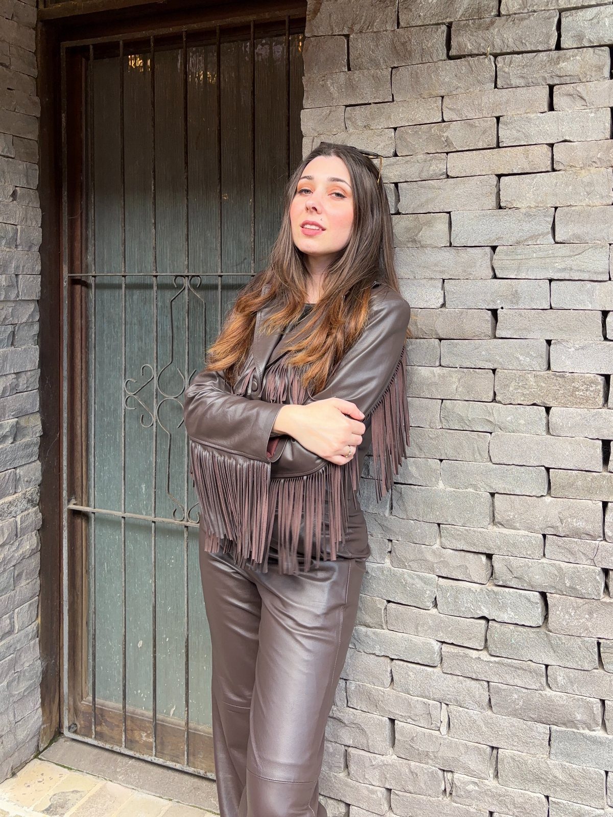 Woman wearing a brown leather fringe jacket and matching brown leather pants.