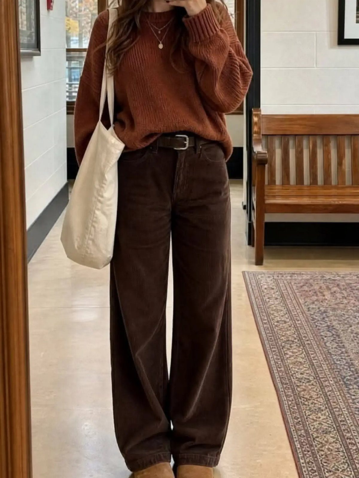 Person wearing rust sweater and dark brown wide-leg corduroy pants in a hallway