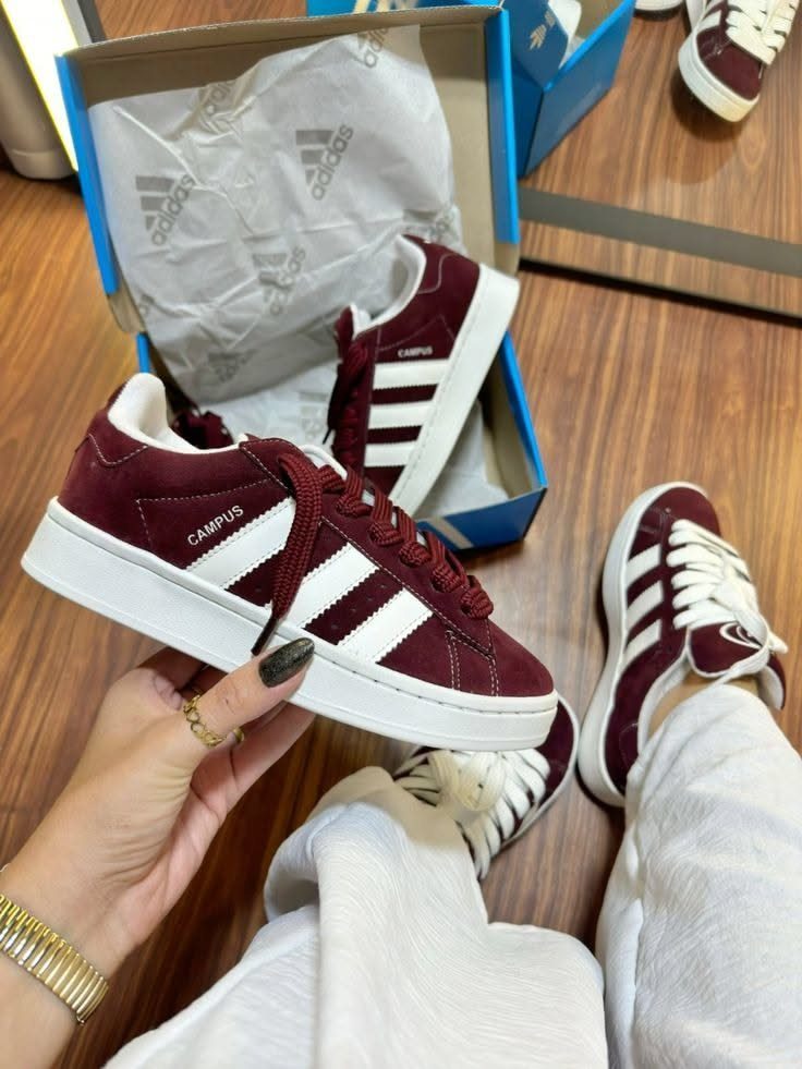 Burgundy Adidas Campus Outfit Ideas: 5 Ways to Wear Them 3 Burgundy Adidas Campus sneakers held by a hand wearing gold rings and bracelet.