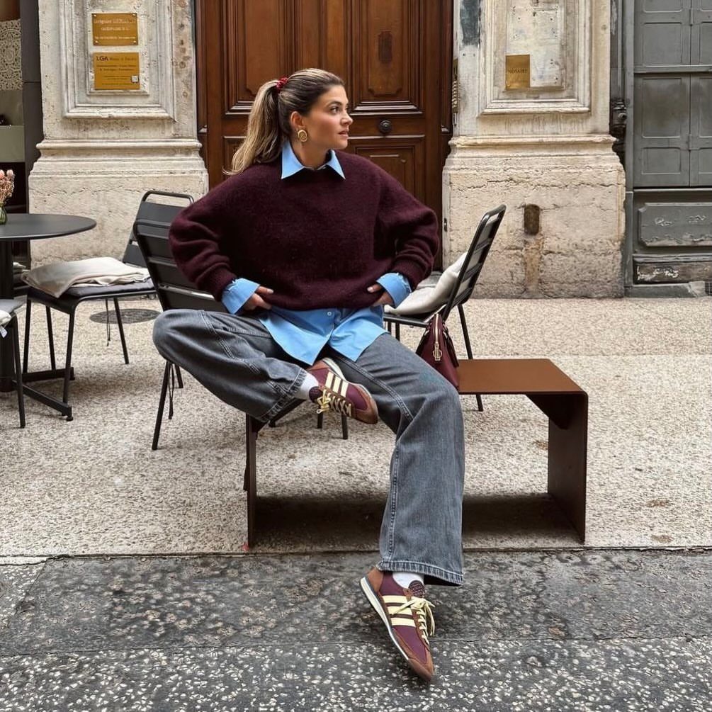Burgundy Adidas Campus Outfit Ideas: 5 Ways to Wear Them 4 Woman wearing burgundy sneakers and grey wide-leg jeans sitting on a city street.