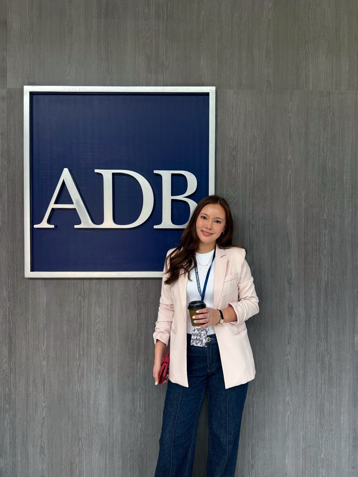 Career Fair Outfits for Women: 8 Ideas to Wear 2 Woman wearing a pink blazer and blue jeans standing by an ADB sign.