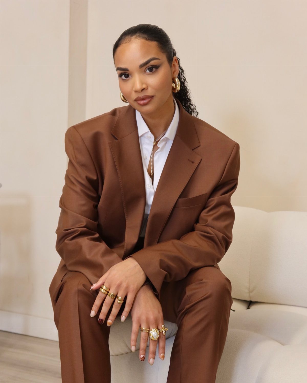 Career Fair Outfits for Women: 8 Ideas to Wear 7 Woman wearing a professional brown oversized suit and white shirt sitting on a sofa.