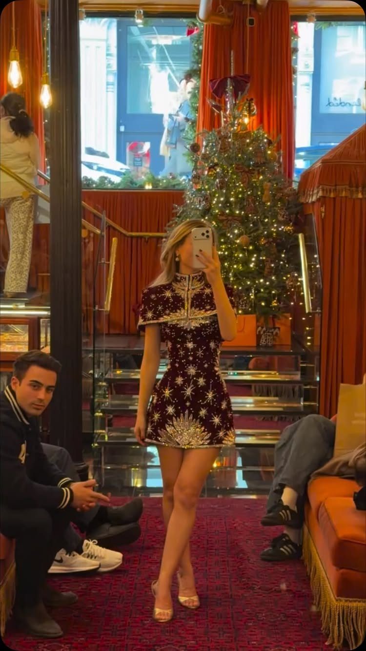 Woman in a red and gold jacquard mini dress posing by a Christmas tree.