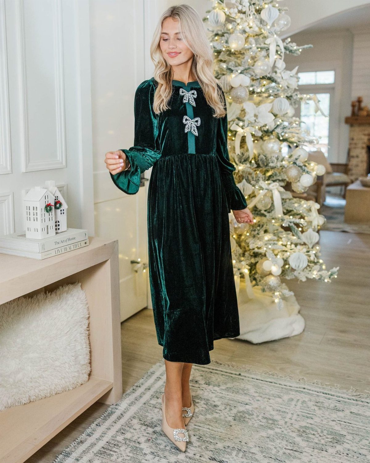 Woman wearing a dark green velvet midi dress standing by a white Christmas tree.