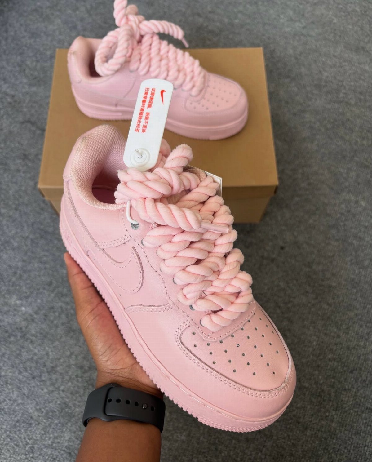Pink leather sneakers with thick pink rope laces held by a hand.