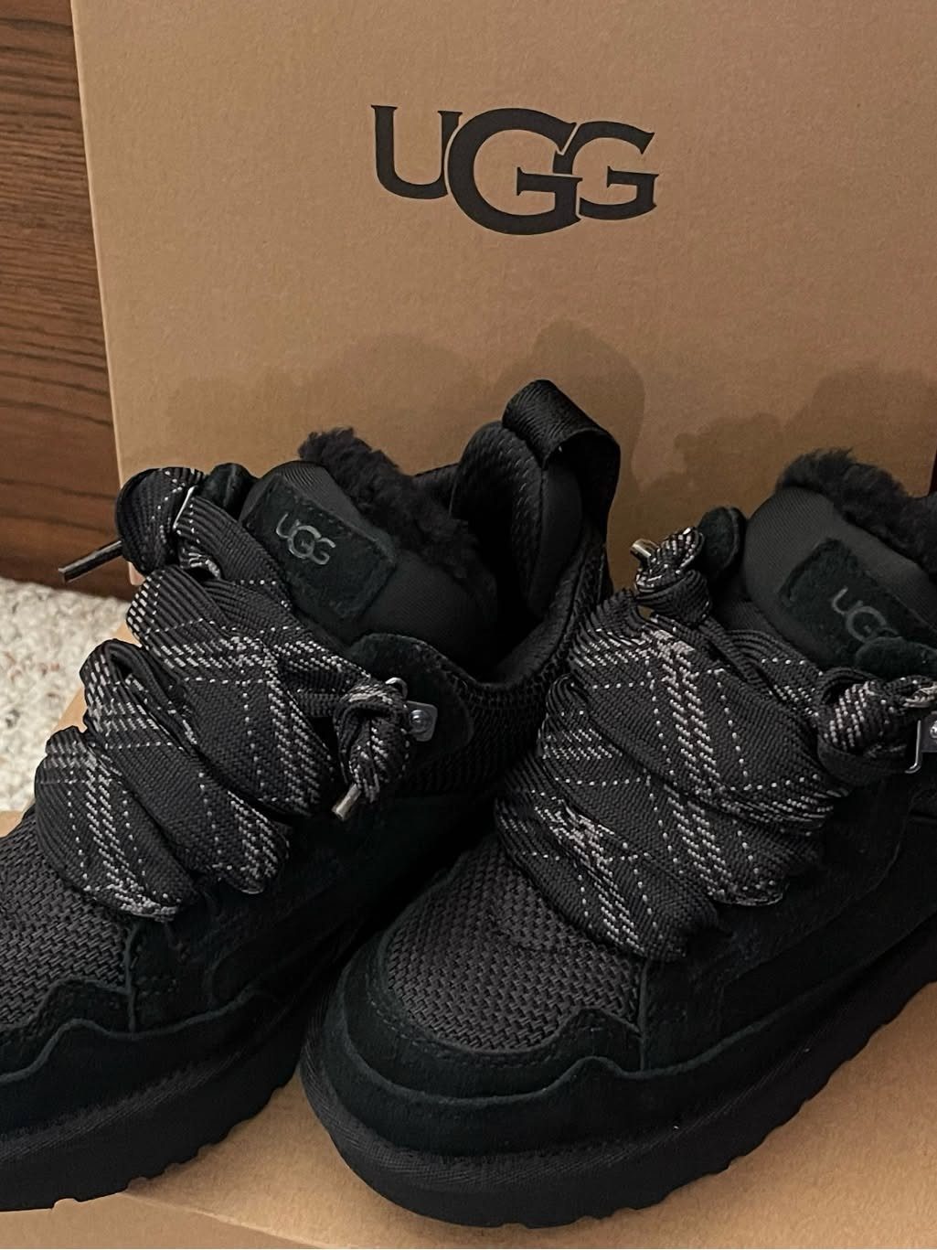 Black UGG sneakers with thick grey patterned flat laces in a shoe box