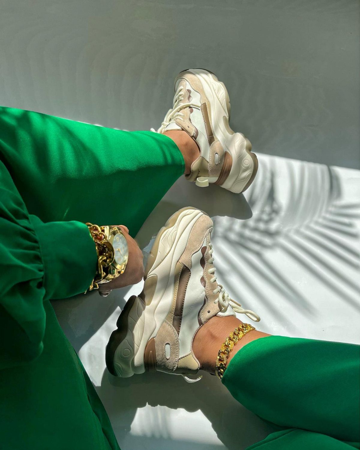 Chunky beige and white platform sneakers worn with bright green trousers and gold jewelry.