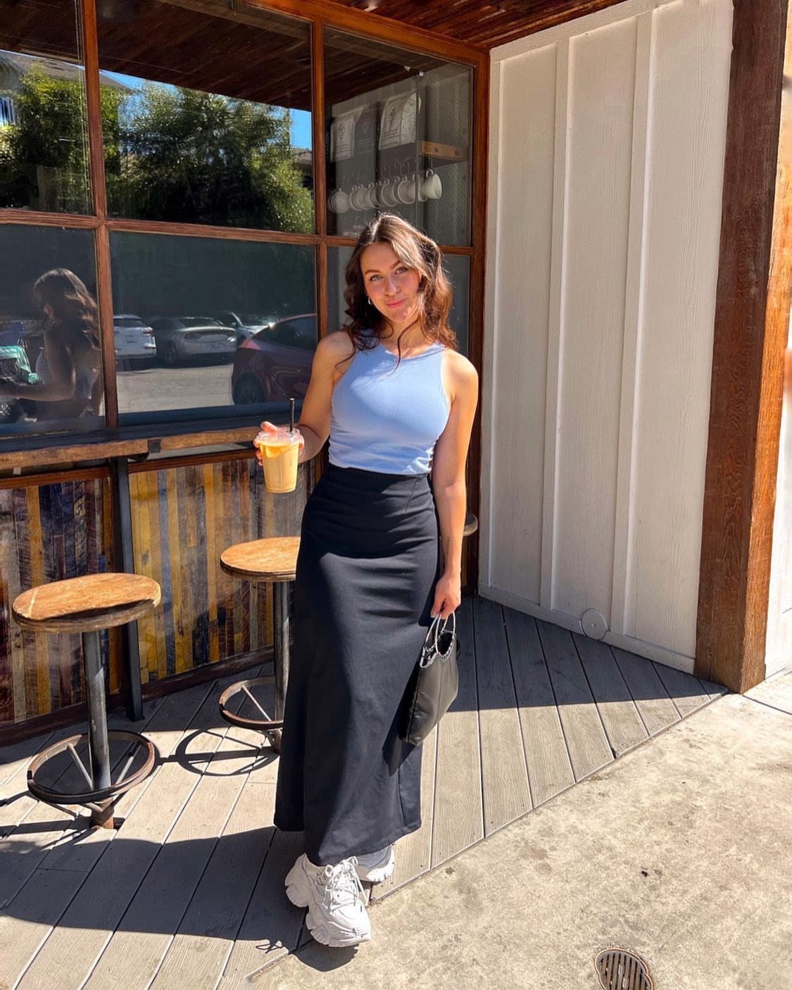 Woman in a blue top and black skirt wearing chunky white streetwear sneakers.