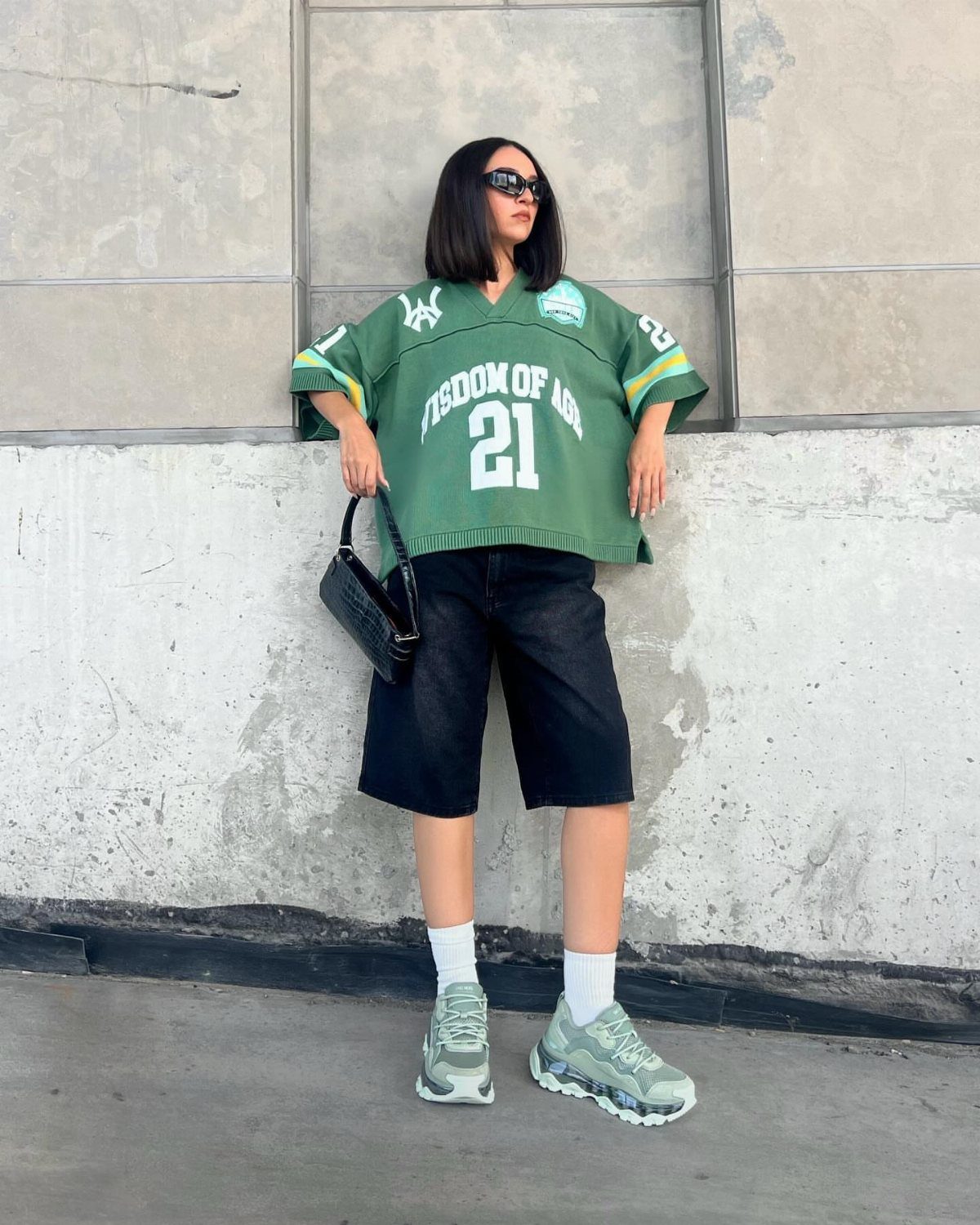 Person wearing chunky light green sneakers and black denim shorts against a concrete wall.