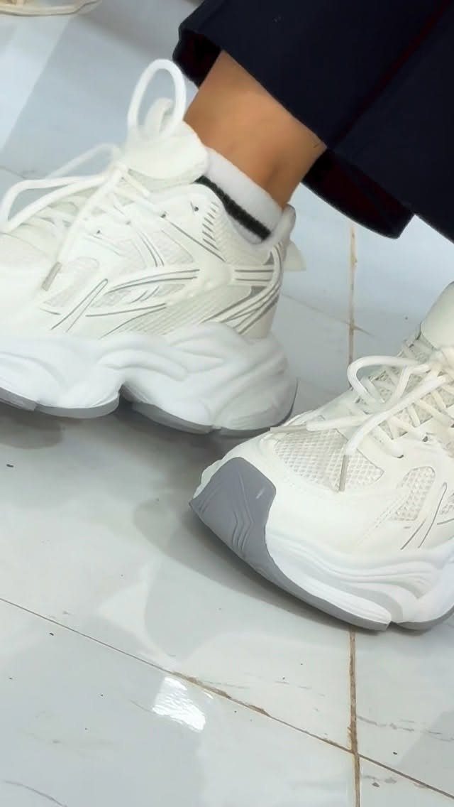 Chunky white streetwear sneakers with thick soles worn with dark trousers and socks.