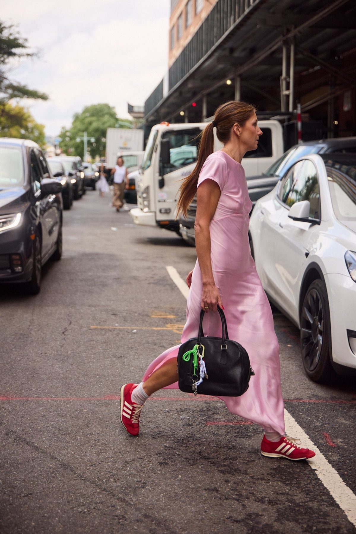 Woman in a light pink satin dress wearing red sneakers walking on street