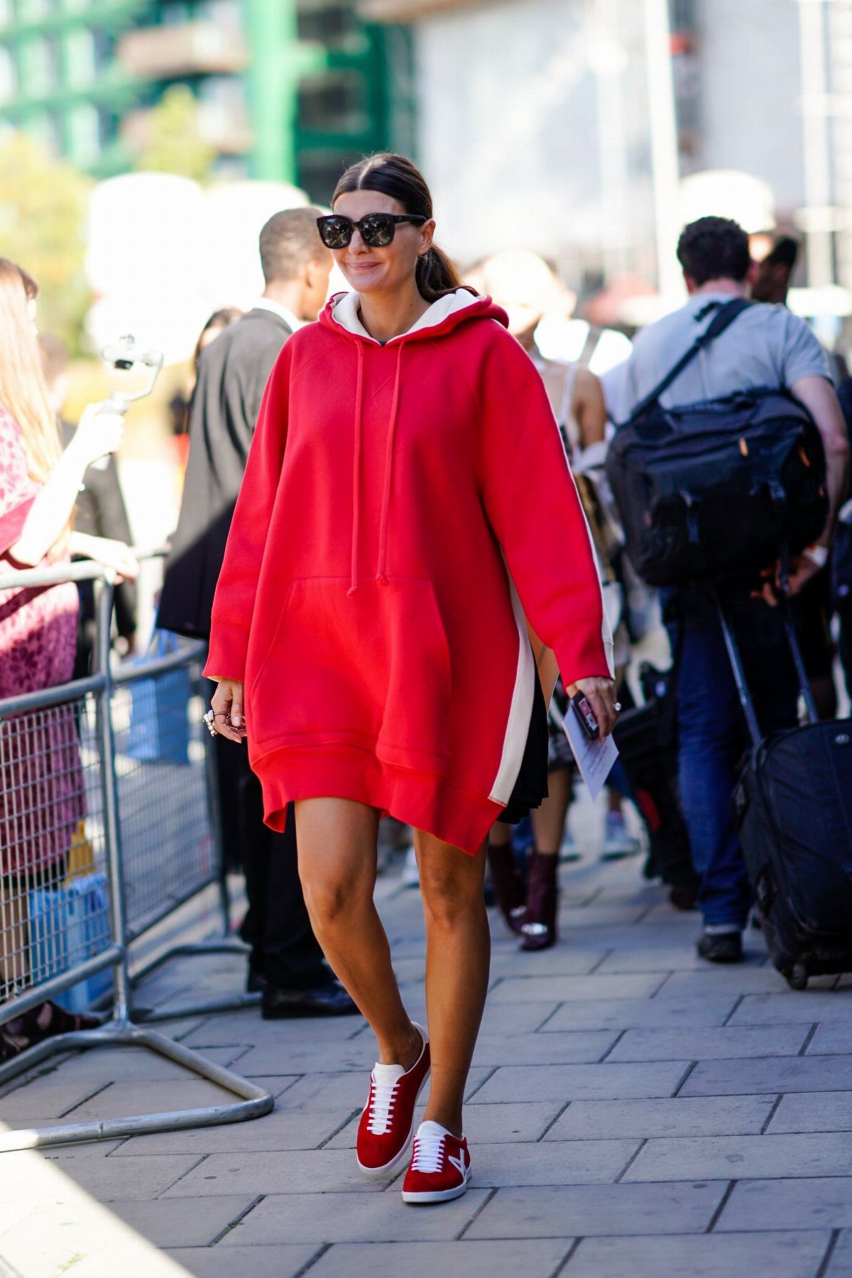 Woman in red oversized hoodie dress and red sneakers walking on city sidewalk