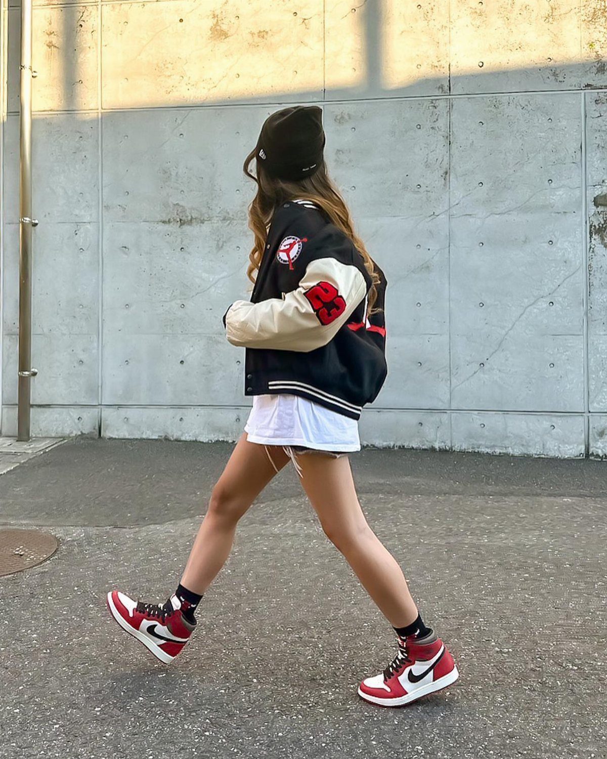 Person wearing red high-top sneakers and an oversized varsity jacket walking by a wall
