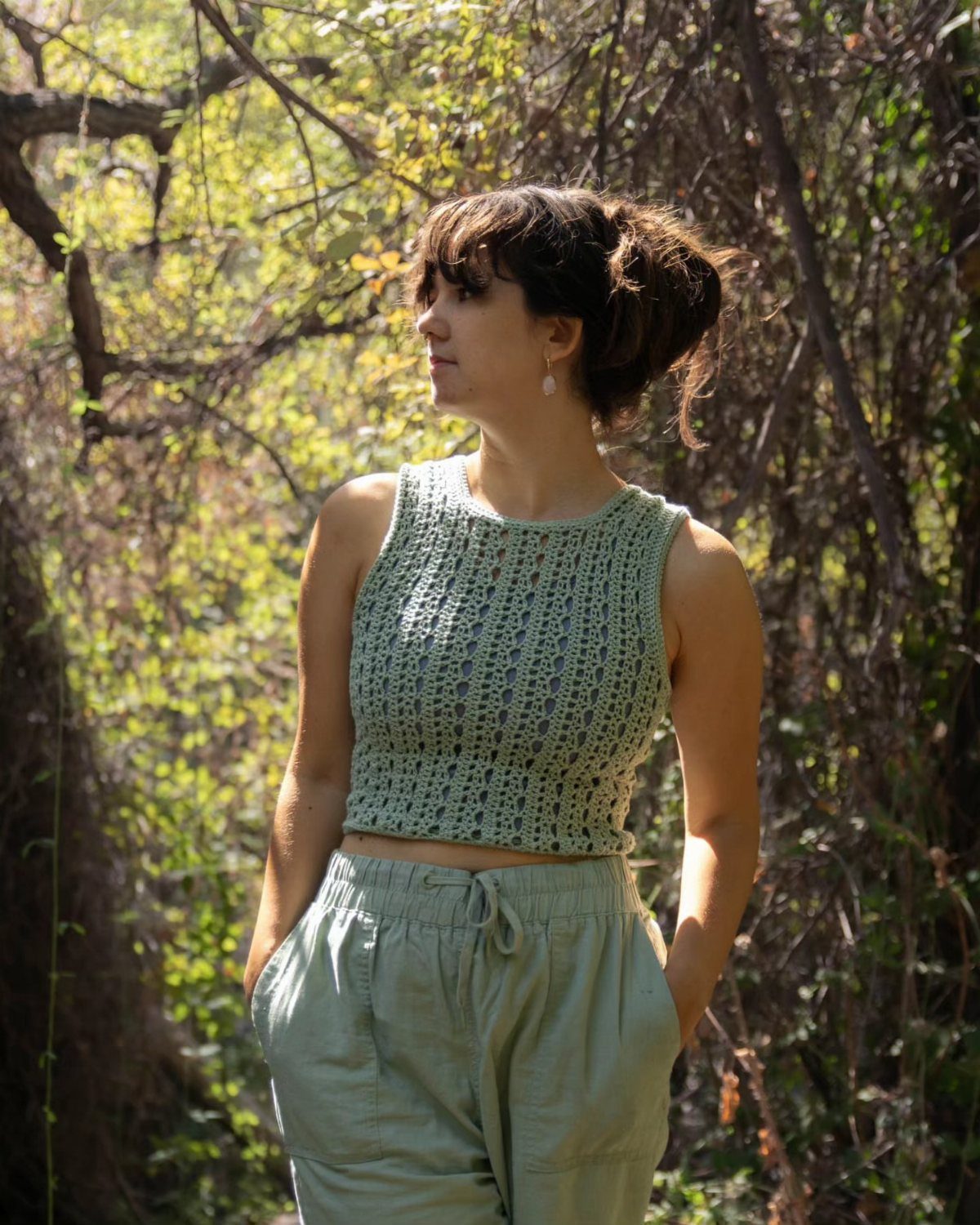 Woman wearing a light green crochet tank top and matching trousers in a forest.