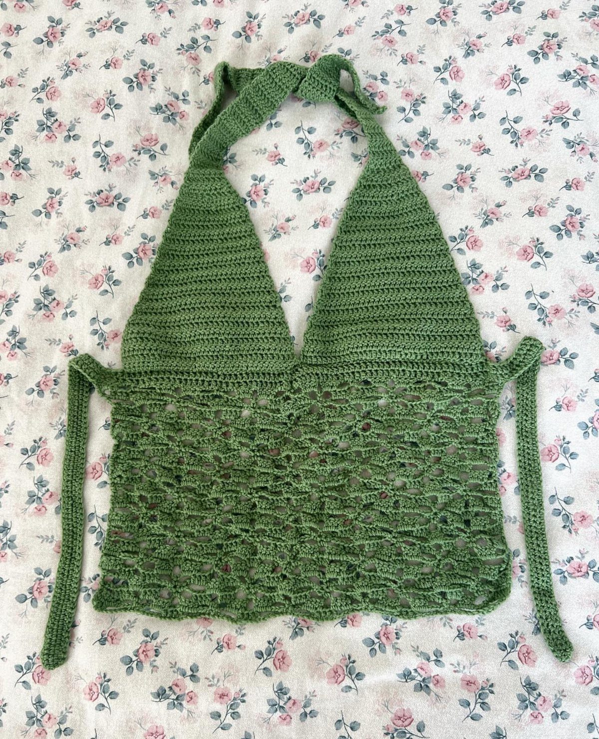 Green crochet halter top with lace detailing on a floral fabric background.