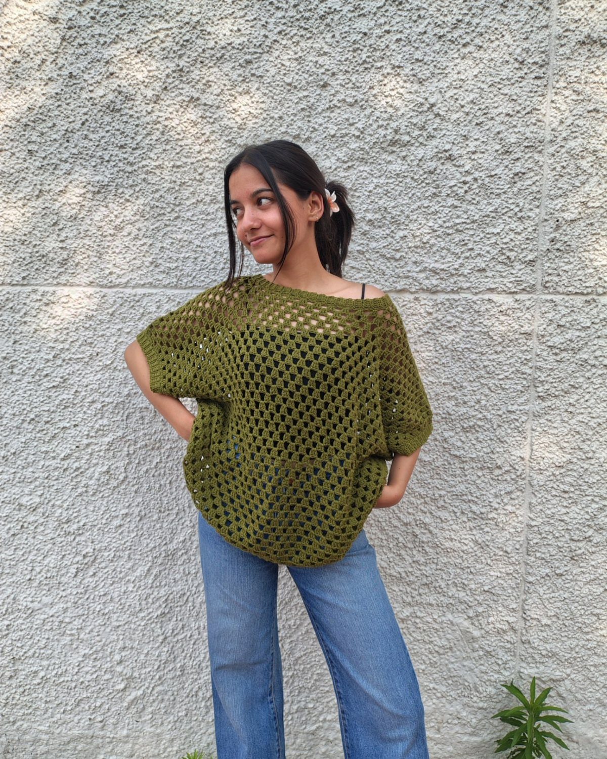 Woman wearing an oversized olive green crochet mesh top and blue jeans.