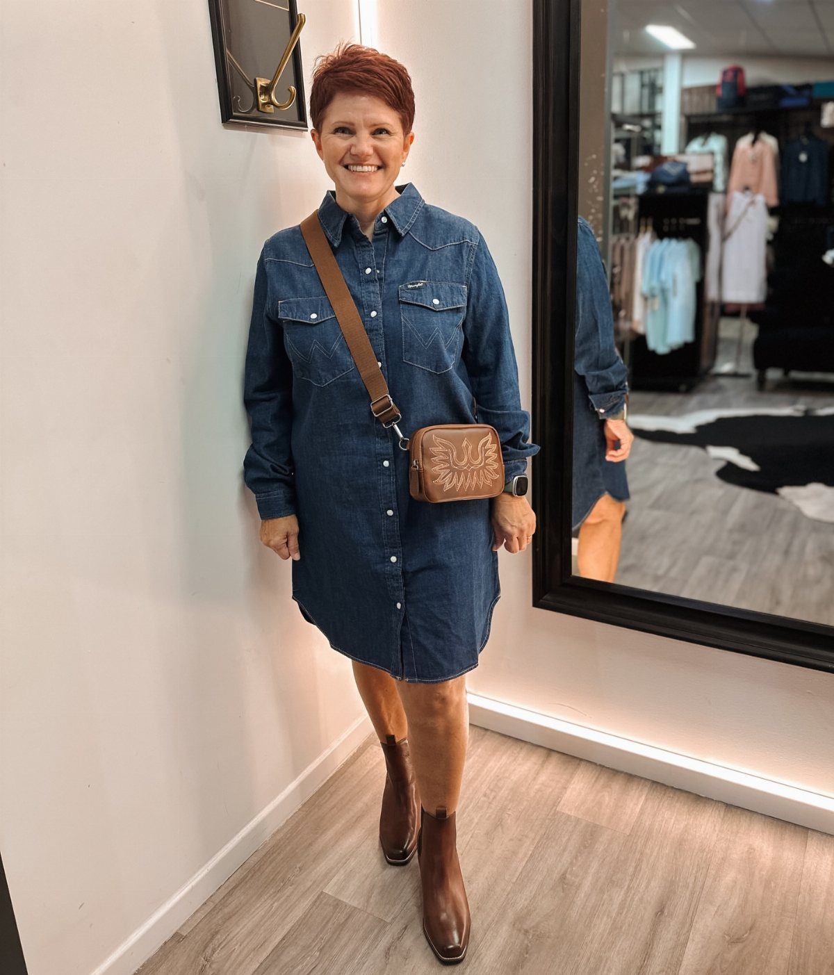 Woman in a blue denim mini dress wearing a brown leather crossbody bag.