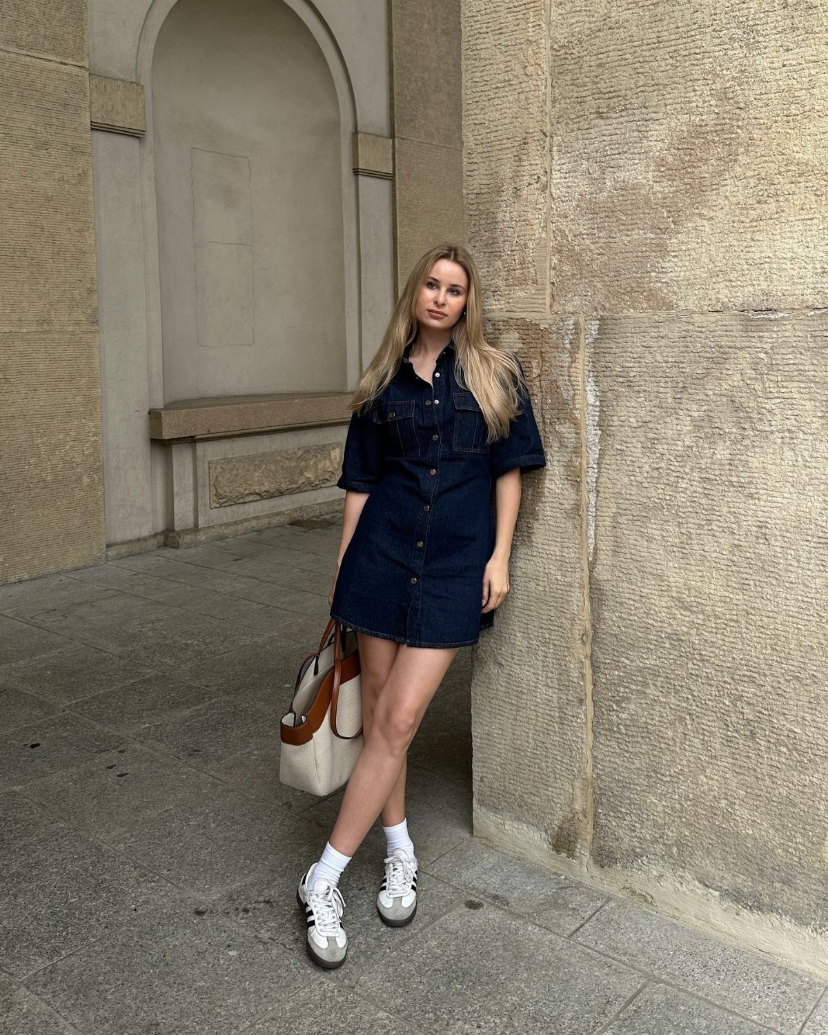 Woman wearing a dark blue denim mini dress with white sneakers and socks.
