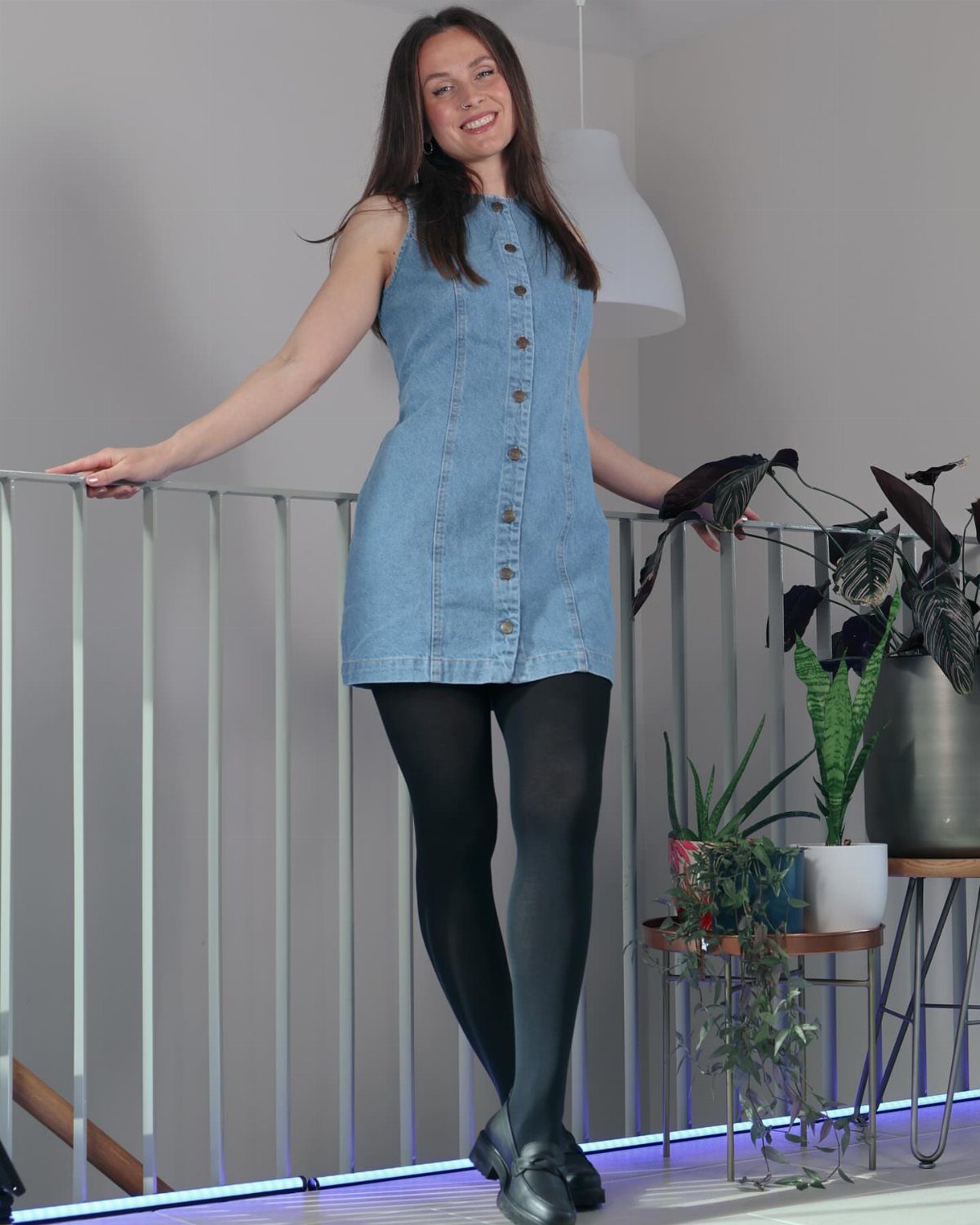 Woman wearing a blue denim mini dress with black tights and black shoes.