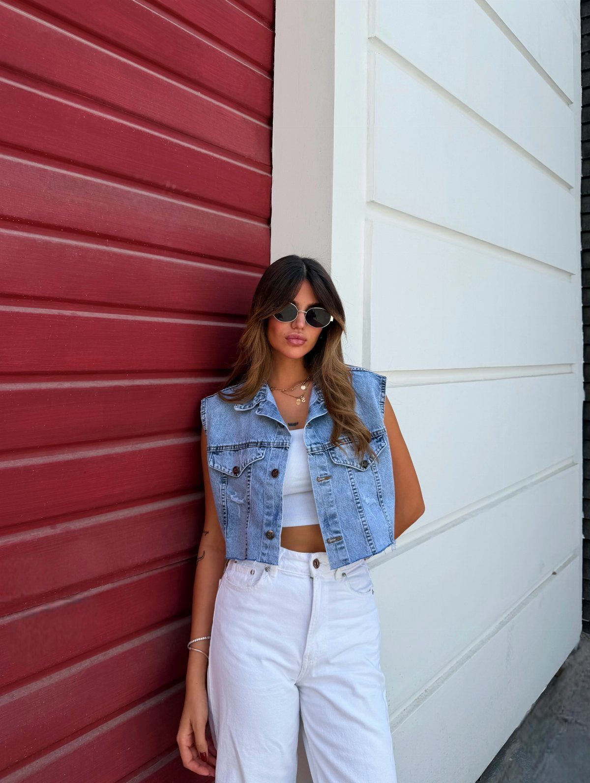 Woman in cropped blue denim vest and white pants posing by colorful walls