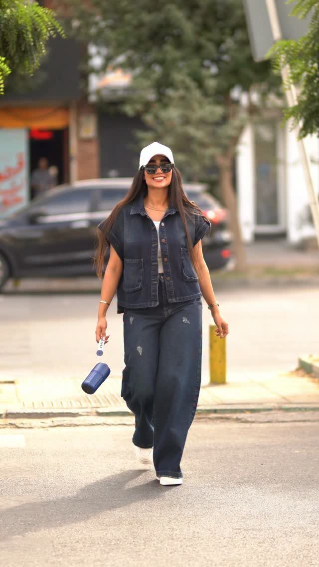 Woman wearing a dark blue denim vest and matching wide-leg jeans walking outdoors.