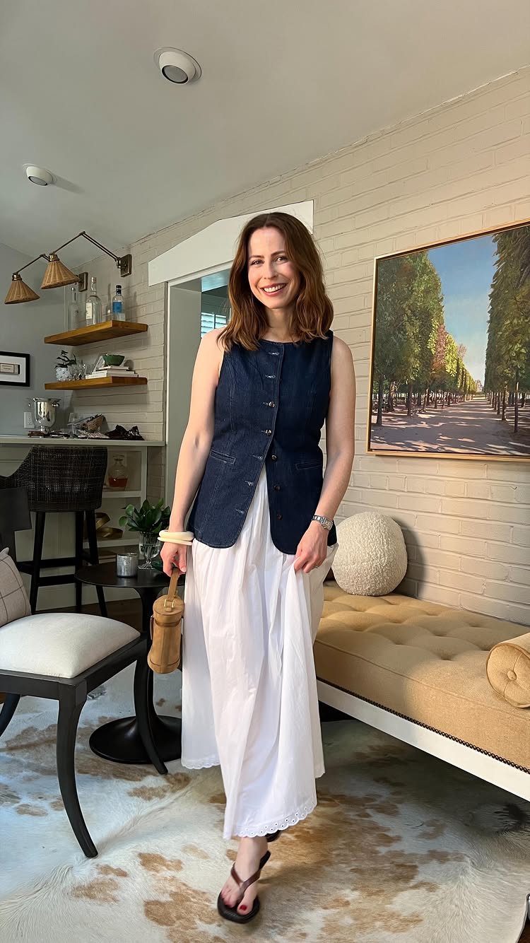 Woman wearing a dark blue denim vest over a long white slip dress.