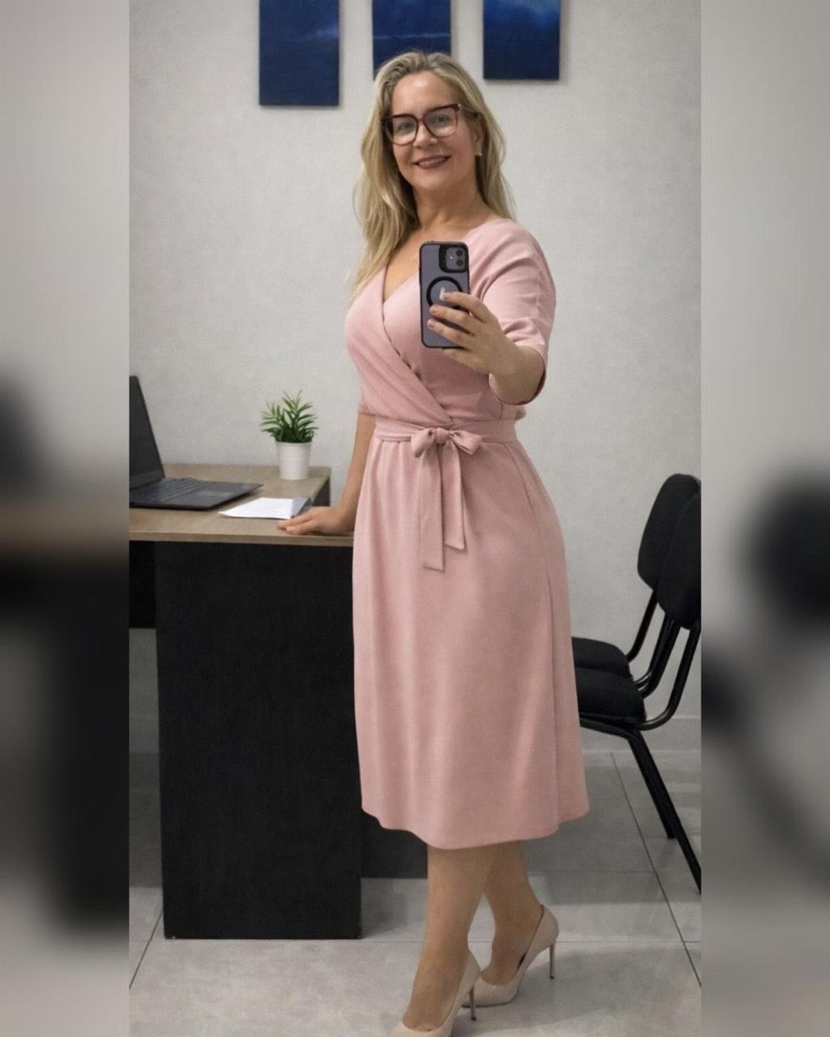 Woman wearing a light pink wrap dress and beige heels in an office.