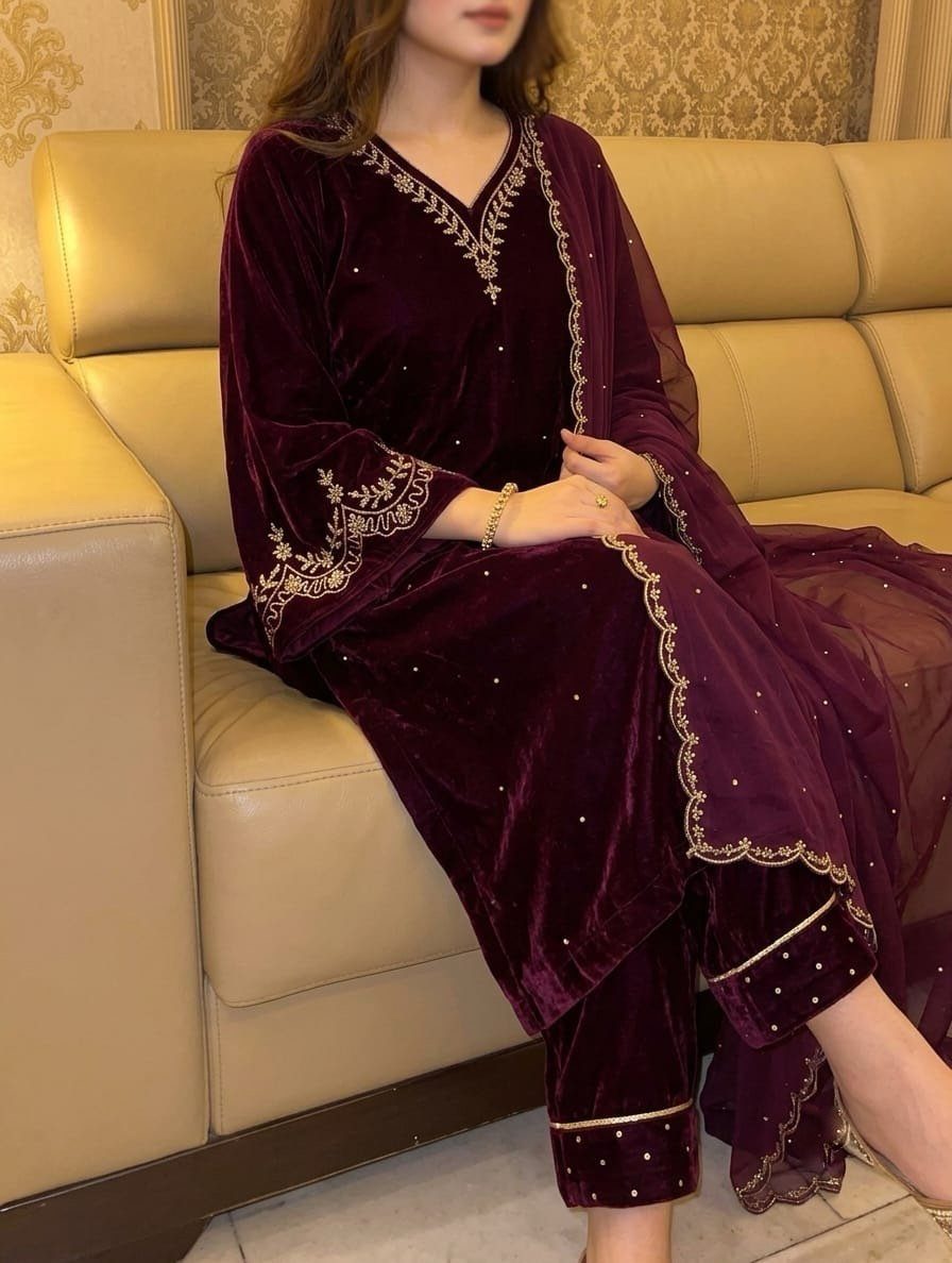 Burgundy velvet salwar kameez with gold embroidery worn by a woman on a sofa