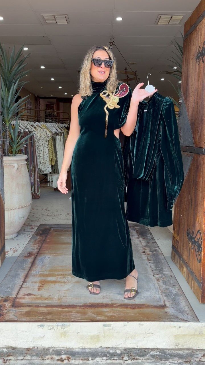 Woman in an emerald green one-shoulder velvet gown with gold shoulder embellishments.