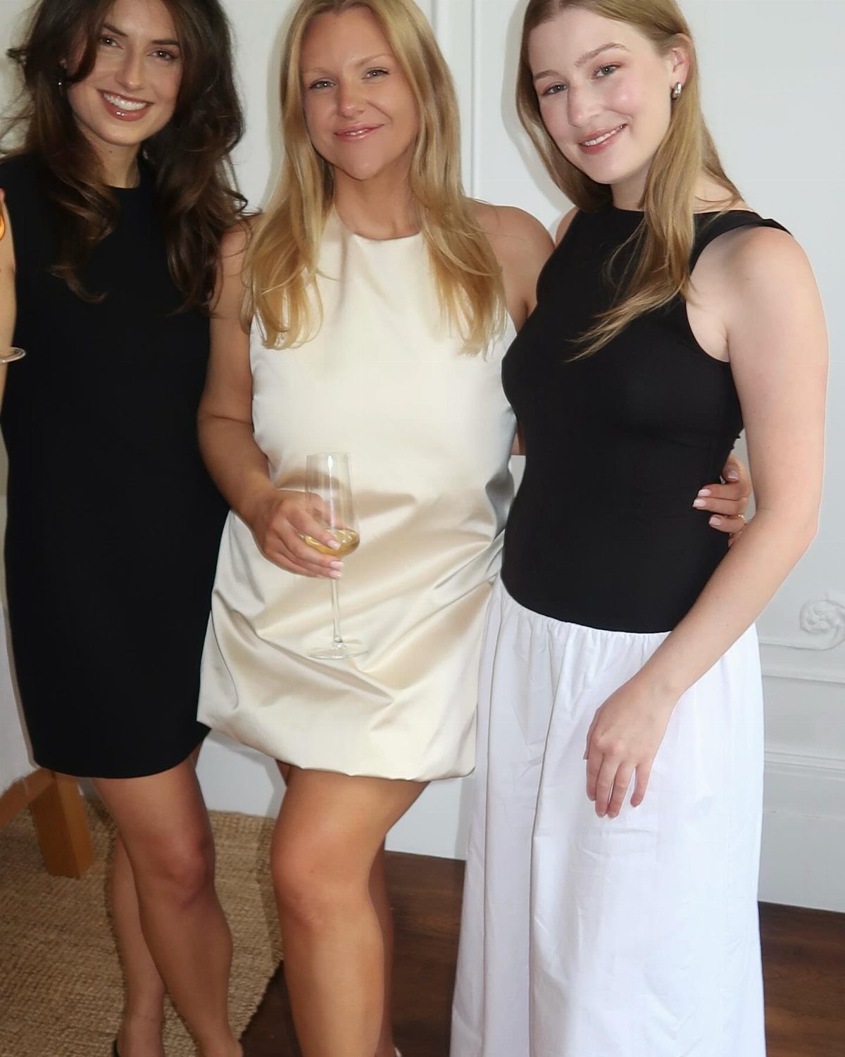 Three women in cocktail and casual attire posing together at an indoor gathering.