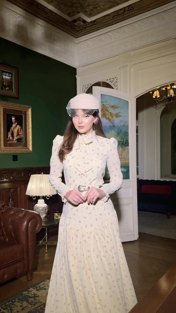 Woman in a retro white floral dress and pillbox hat in a classic room