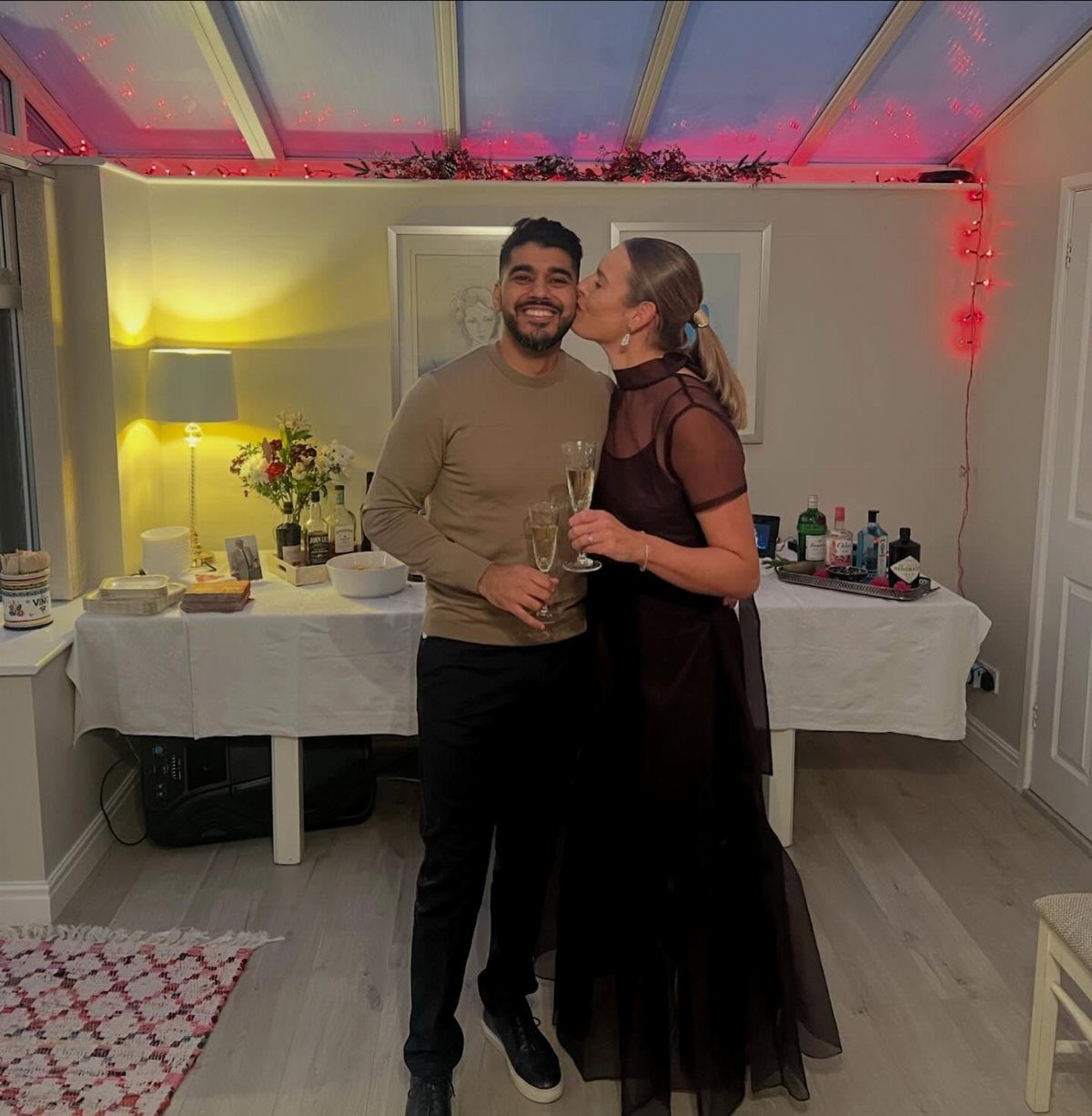 Couple kissing at a party, woman wearing a black sheer maxi dress.