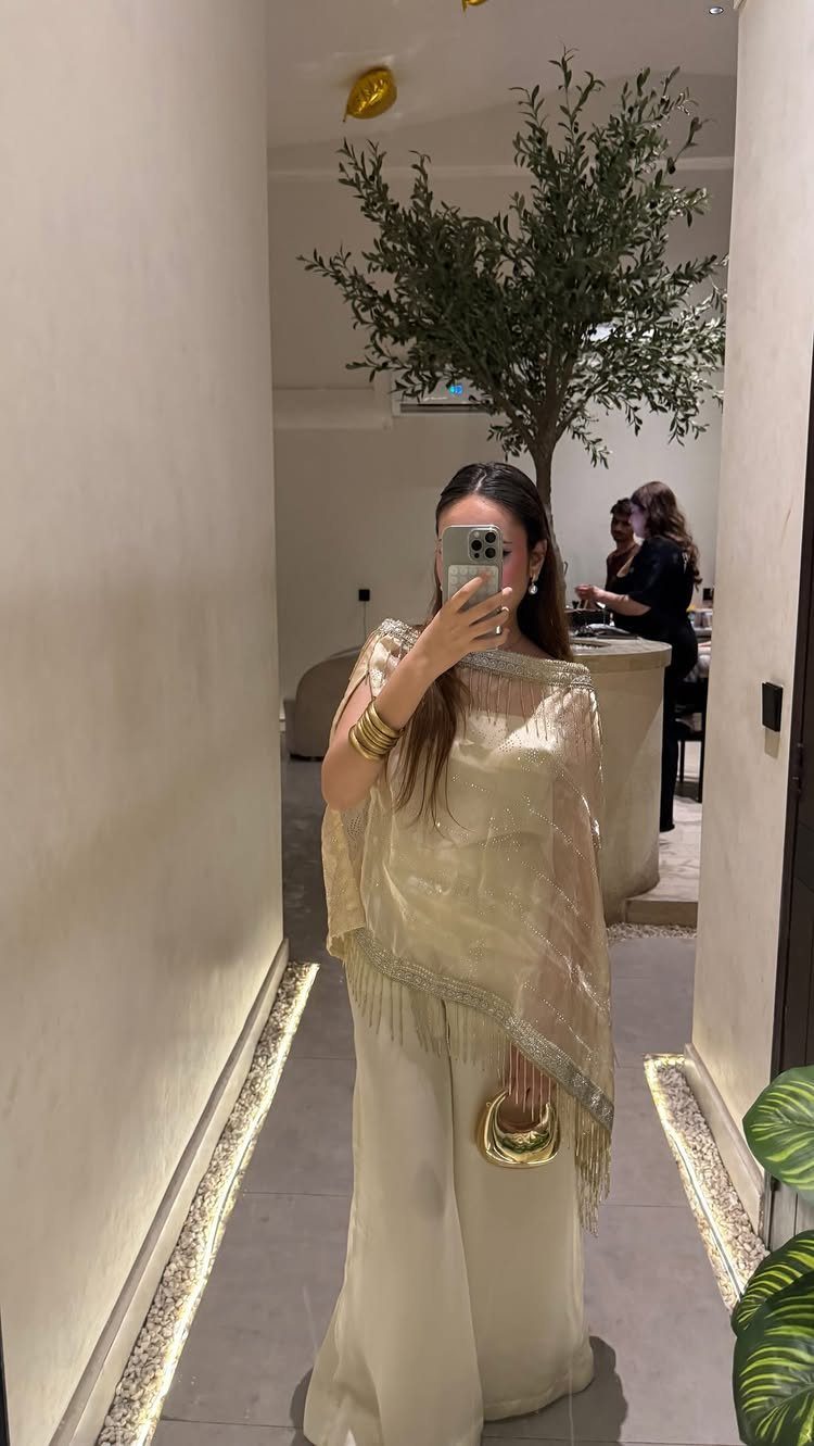 Woman in a shimmering gold fringed top and wide-leg trousers taking a selfie.