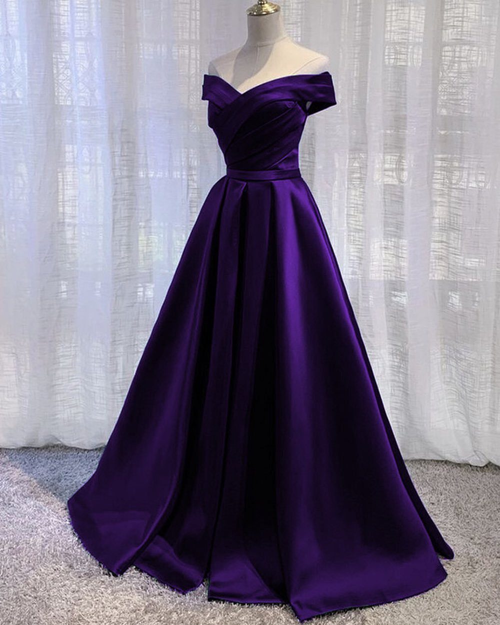 Evening Dress Luxury: 9 Gown Ideas in Satin and Sequins 8 Purple satin off-the-shoulder gown on a mannequin against white sheer curtains