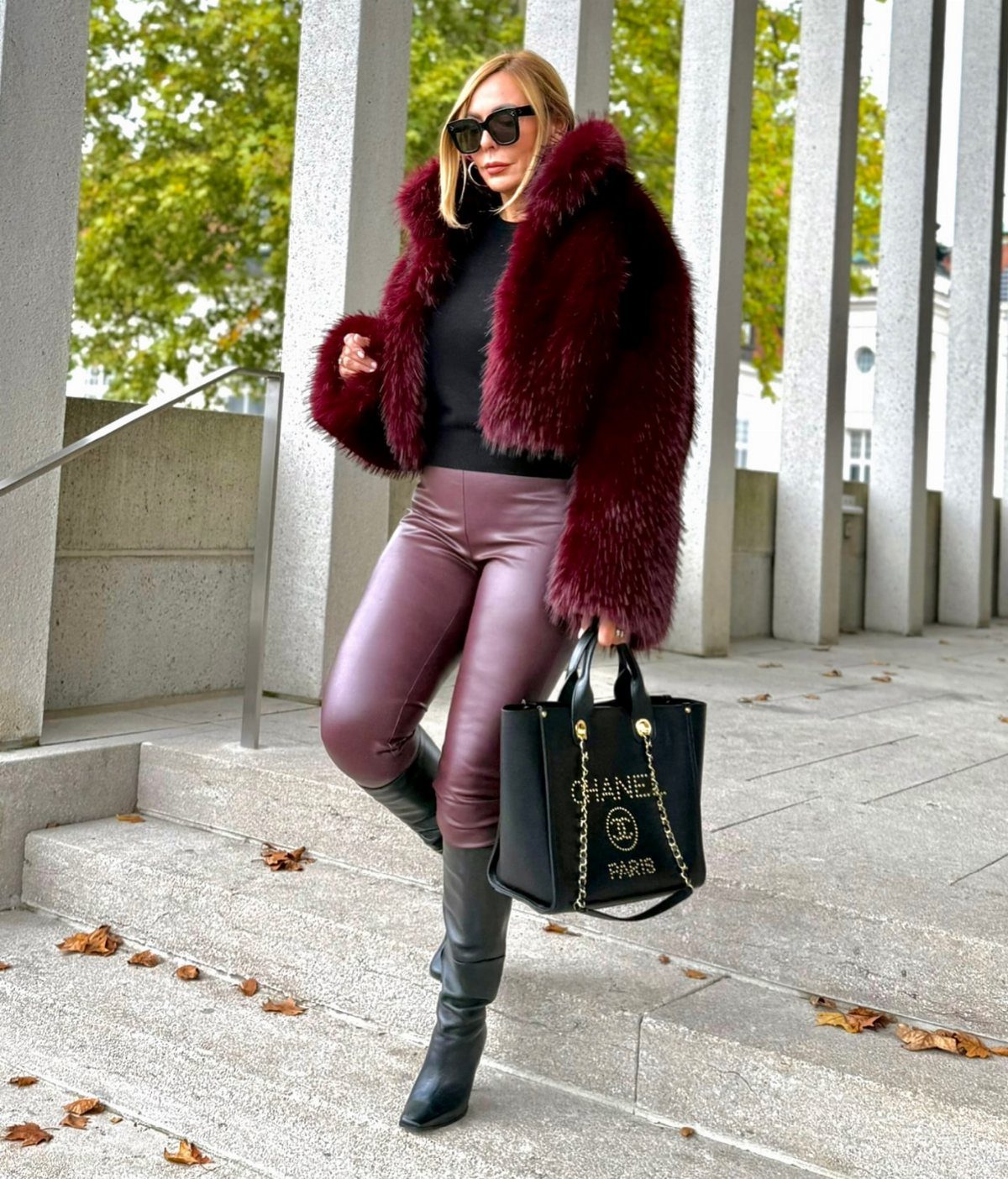 Woman wearing a burgundy faux-fur coat and leather pants standing on concrete steps.