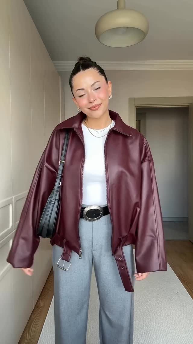 Woman wearing a burgundy leather jacket with white shirt and grey trousers.