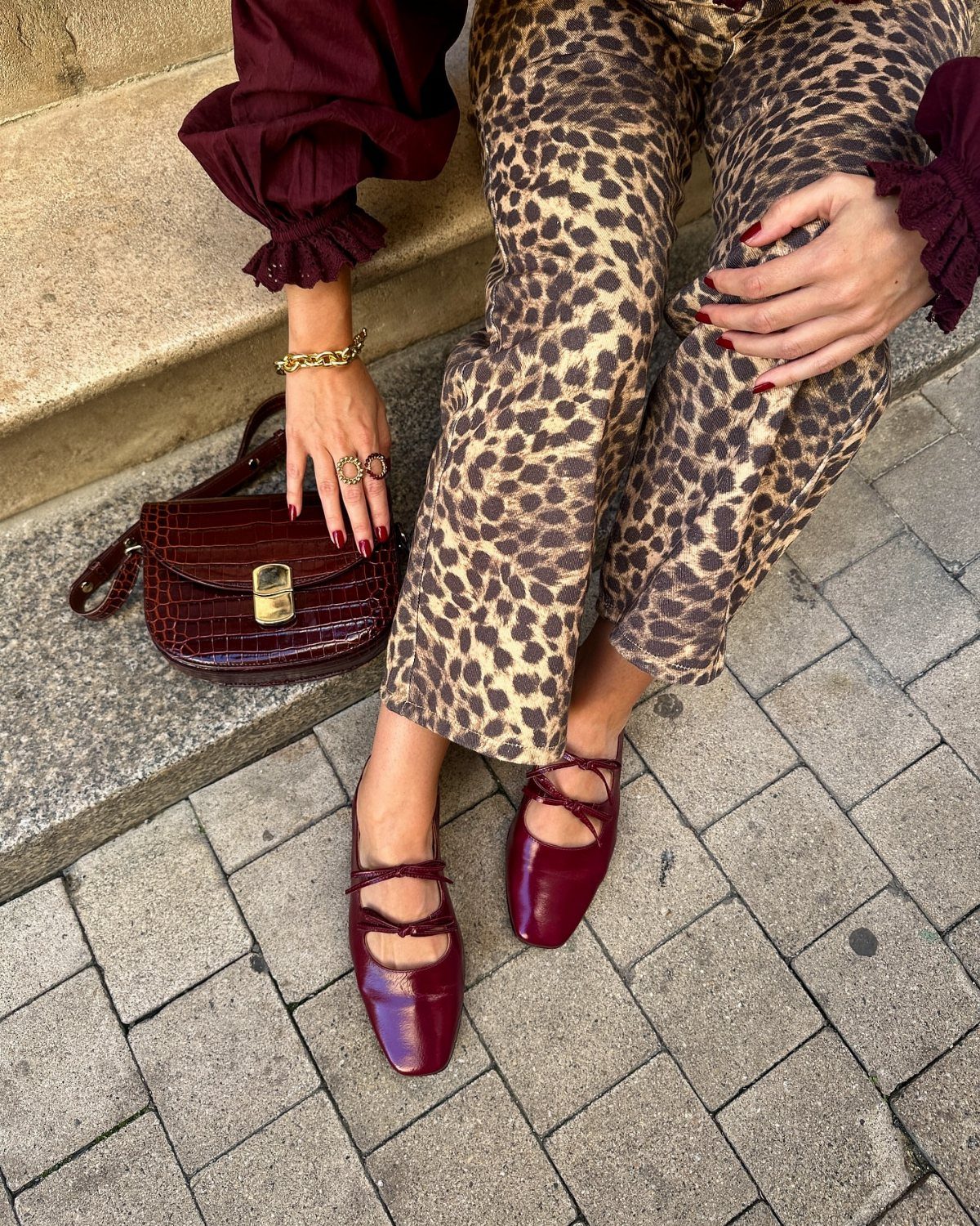 Woman wearing burgundy blouse and shoes with leopard print pants and burgundy handbag.