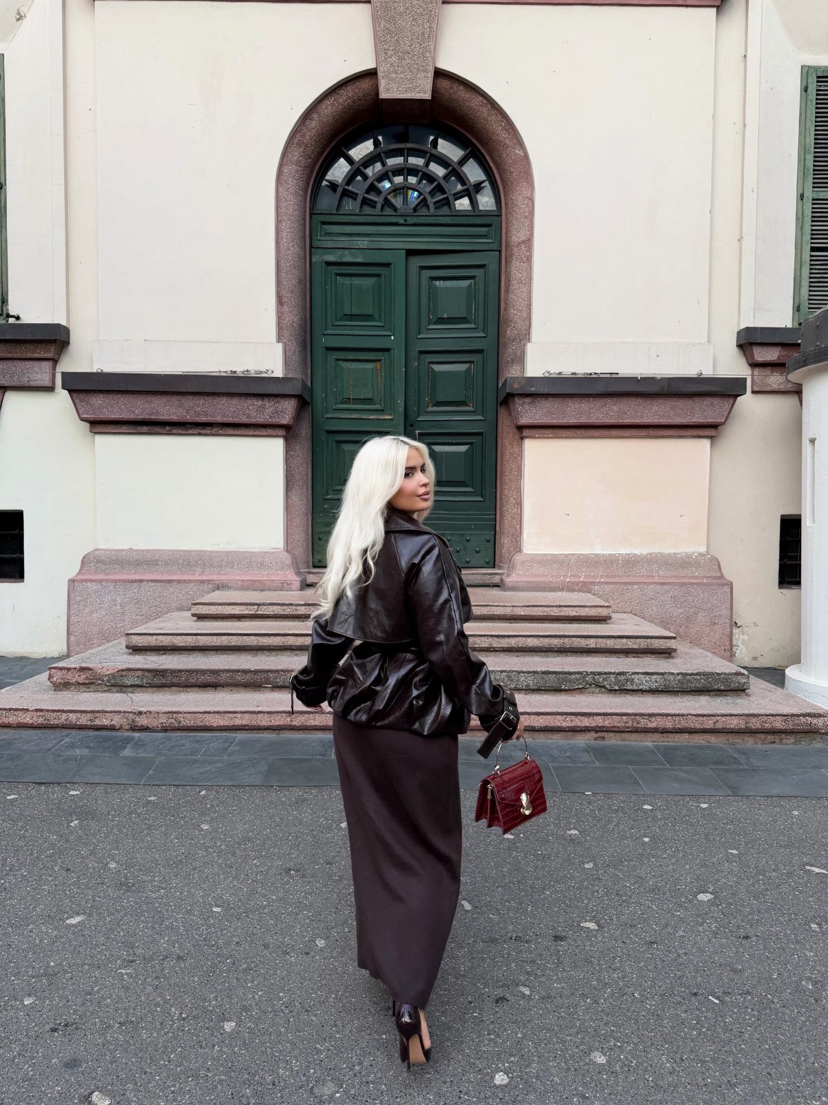 Woman wearing a burgundy skirt and leather jacket standing before a green door