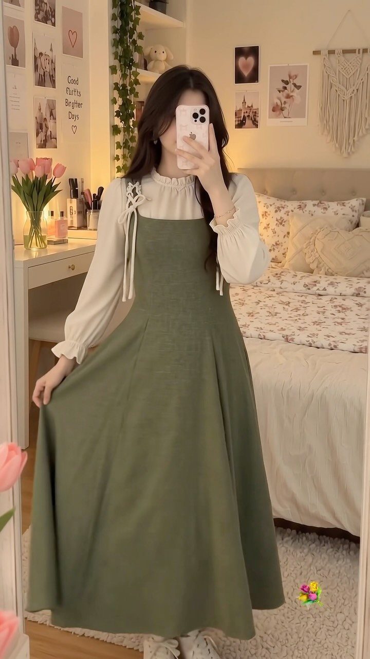 Fall Picnic Outfit Ideas: 10 Cozy Looks to Wear 3 Woman wearing an olive green maxi pinafore dress over a white long-sleeved blouse.