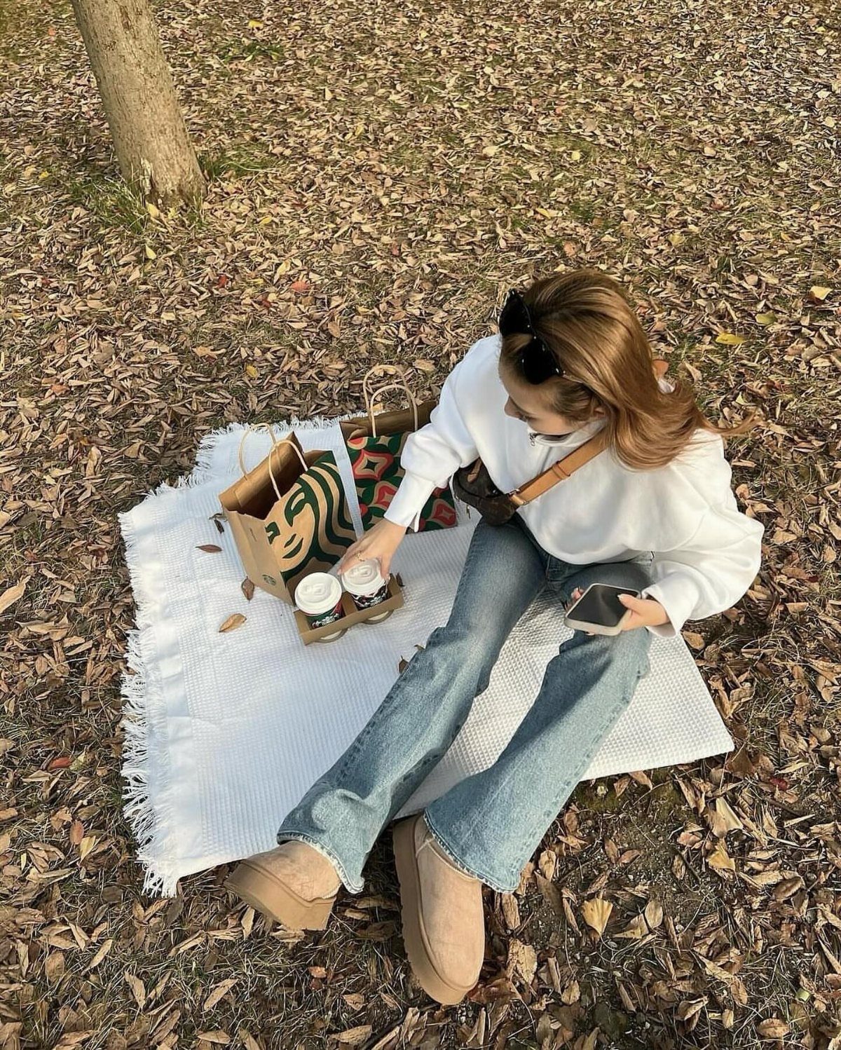 Fall Picnic Outfit Ideas: 10 Cozy Looks to Wear 6 Woman in white top and jeans sitting on a blanket among autumn leaves.