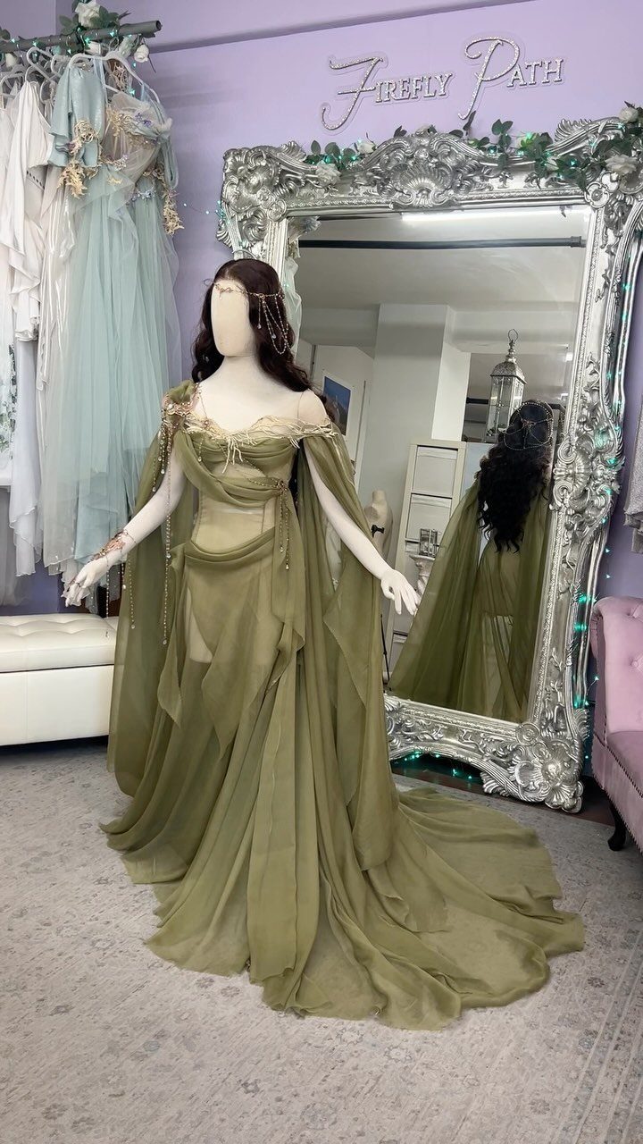 Olive green chiffon gown with flowing sleeves on a mannequin before a mirror.