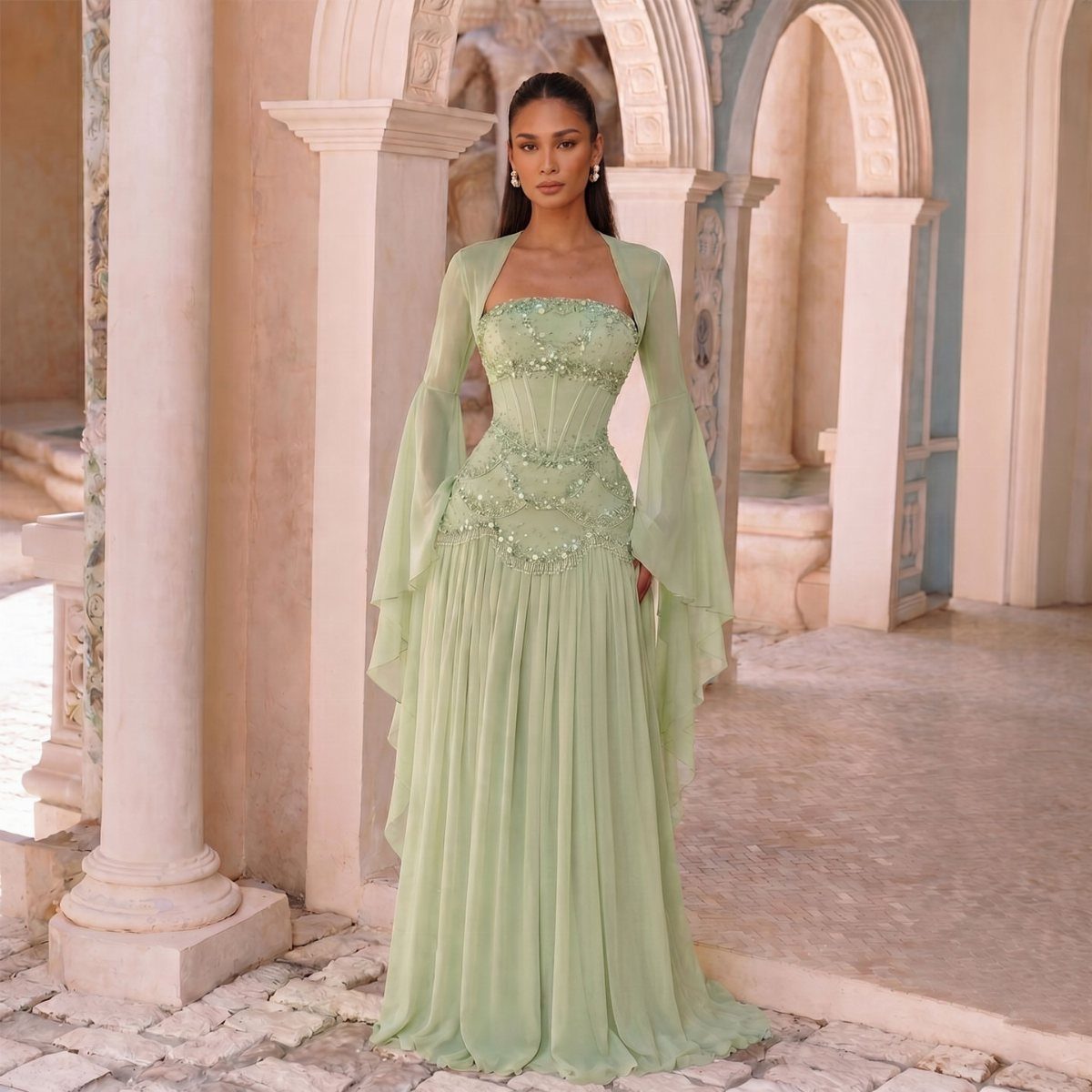 Woman in a pale green beaded chiffon gown with sheer cape sleeves.