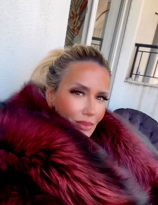 11 Glitz Glam Outfit Ideas with Sequins, Fringe and Fur 1 Woman wearing a voluminous deep red and burgundy faux fur jacket posing outdoors.