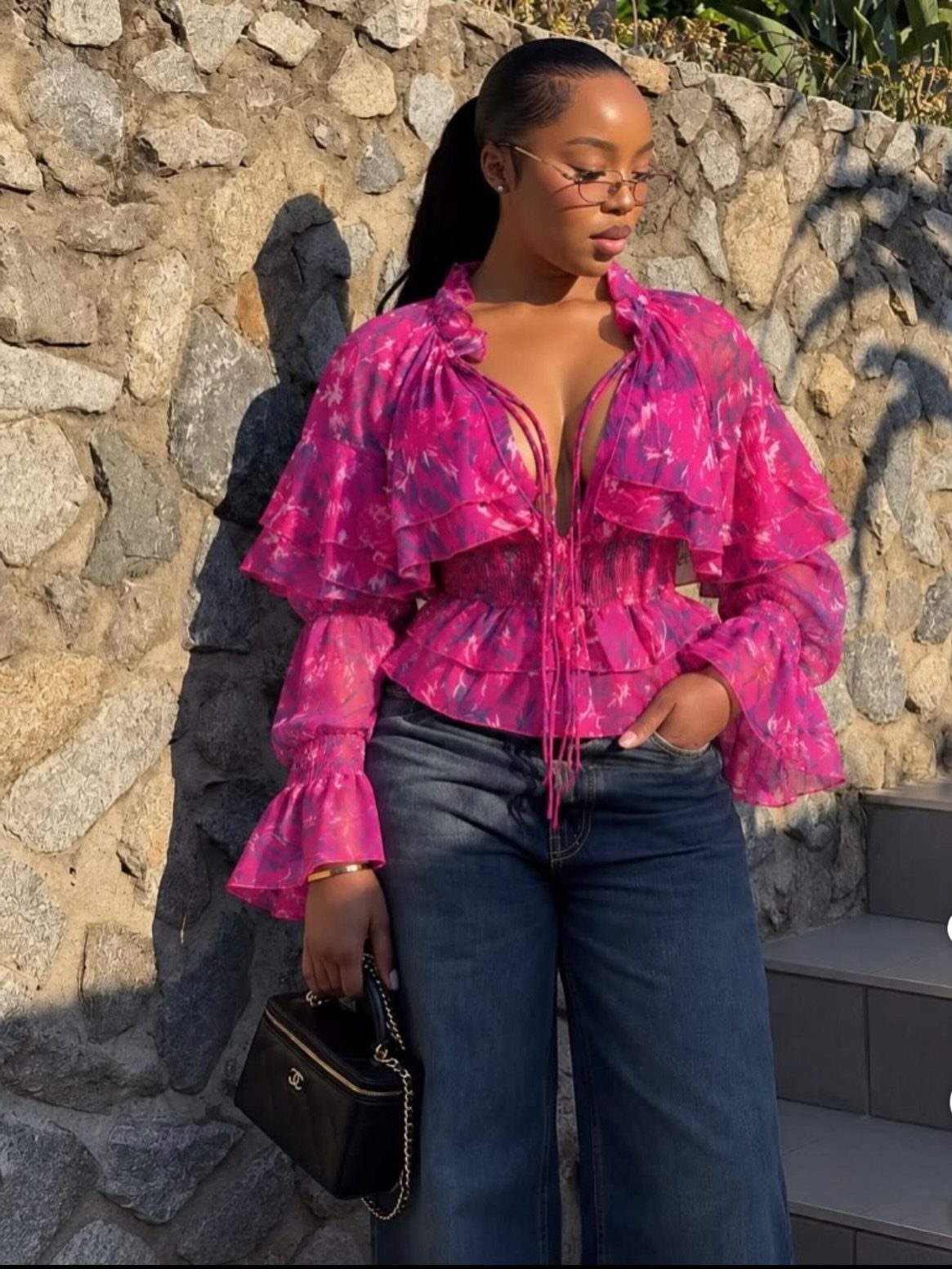 11 Glitz Glam Outfit Ideas with Sequins, Fringe and Fur 2 Woman in a pink floral ruffled blouse and blue jeans holding a black handbag.
