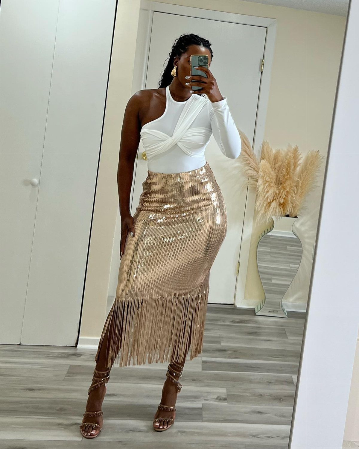 11 Glitz Glam Outfit Ideas with Sequins, Fringe and Fur 10 Woman wearing a white one-shoulder top and a gold sequined high-rise fringe skirt.