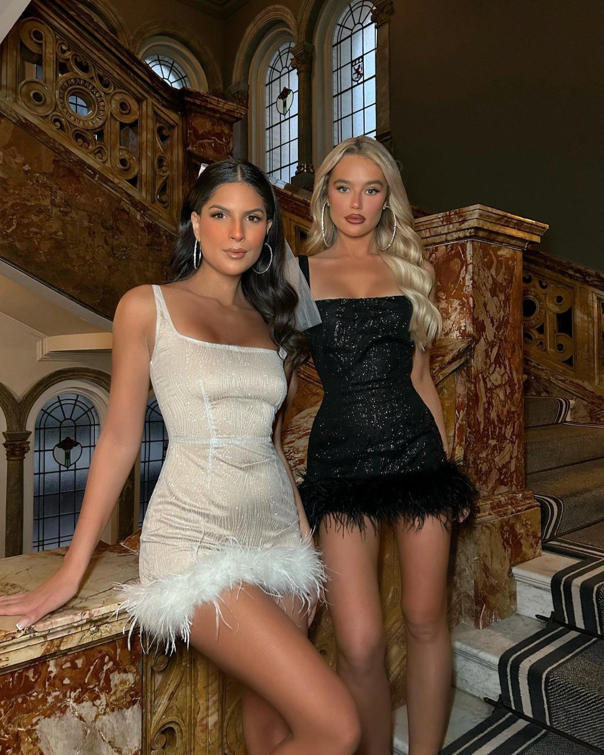 11 Glitz Glam Outfit Ideas with Sequins, Fringe and Fur 9 Two women in sparkly mini dresses with feather hems posing on marble stairs.