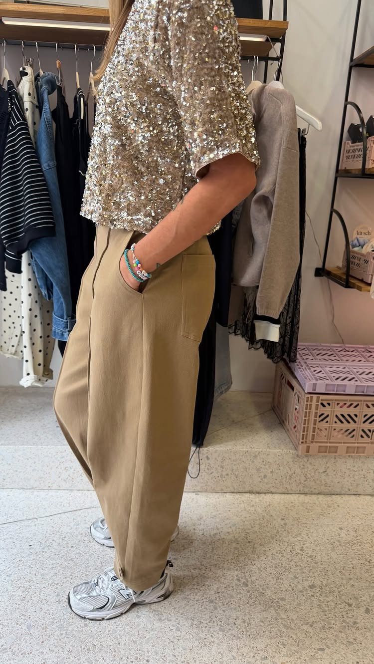 11 Glitz Glam Outfit Ideas with Sequins, Fringe and Fur 3 Gold sequined top paired with loose tan trousers in a clothing store setting.