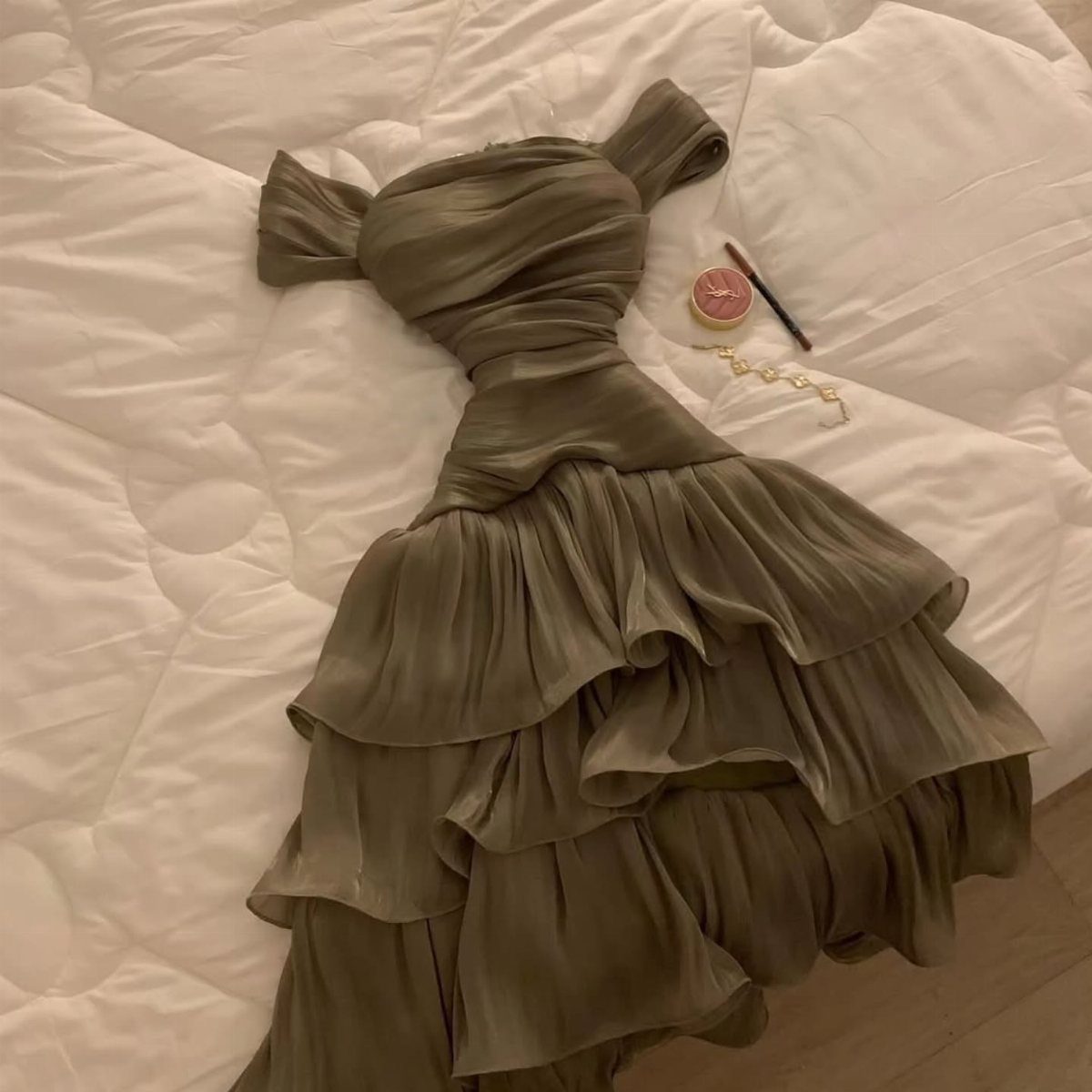 Olive green strapless dress with ruffled tiers and a train on white bedding
